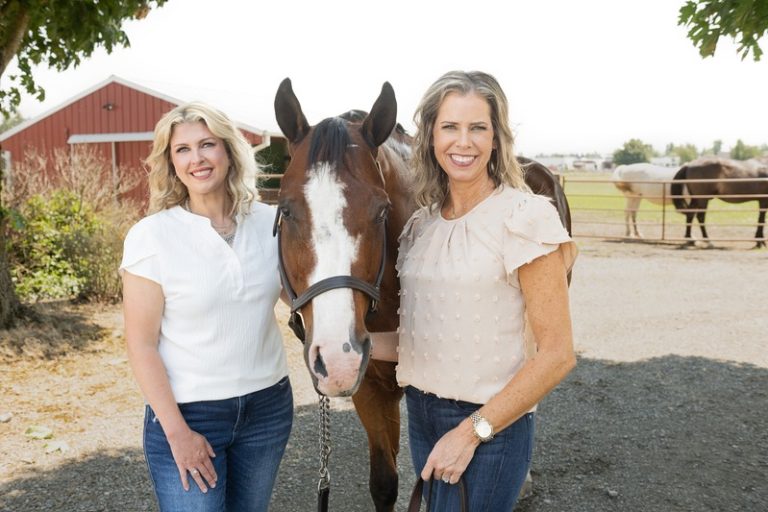 Brandi Coplen and Tresie Wiersma, Whatcom County equestrian Realtors, with a horse at a red barn